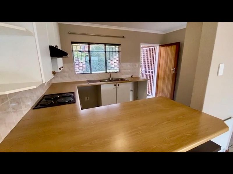 A functional kitchen featuring laminate countertops, a built-in electric hob, extractor fan, and stainless steel sink, with direct access to an exterior security gate.