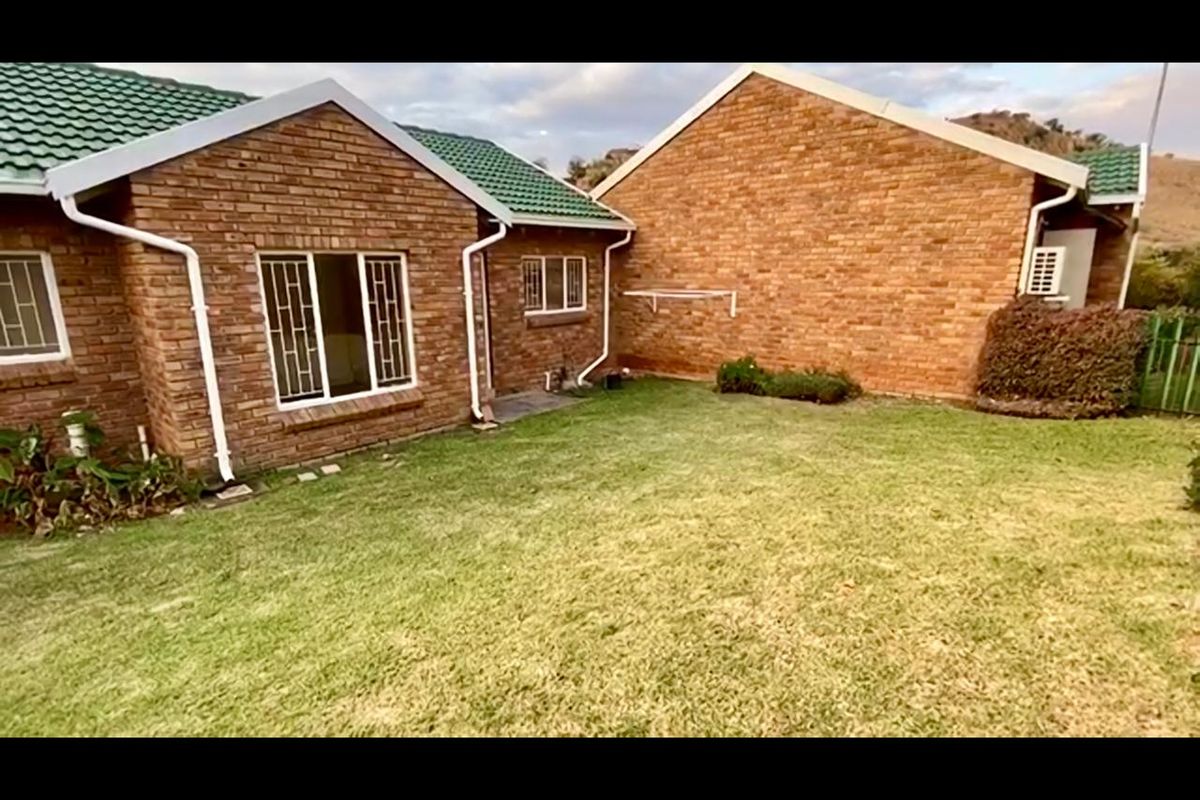A view of the rear exterior of the townhouse featuring face brick walls, green tiled roofing, and a private lawn area.