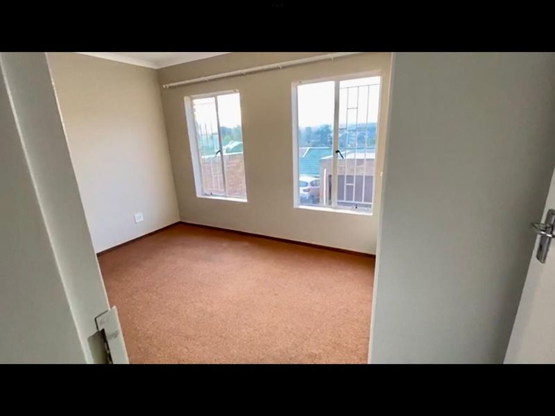 An empty bedroom featuring carpet flooring, security bars on the windows, and neutral wall paint, offering a blank canvas for personalization.
