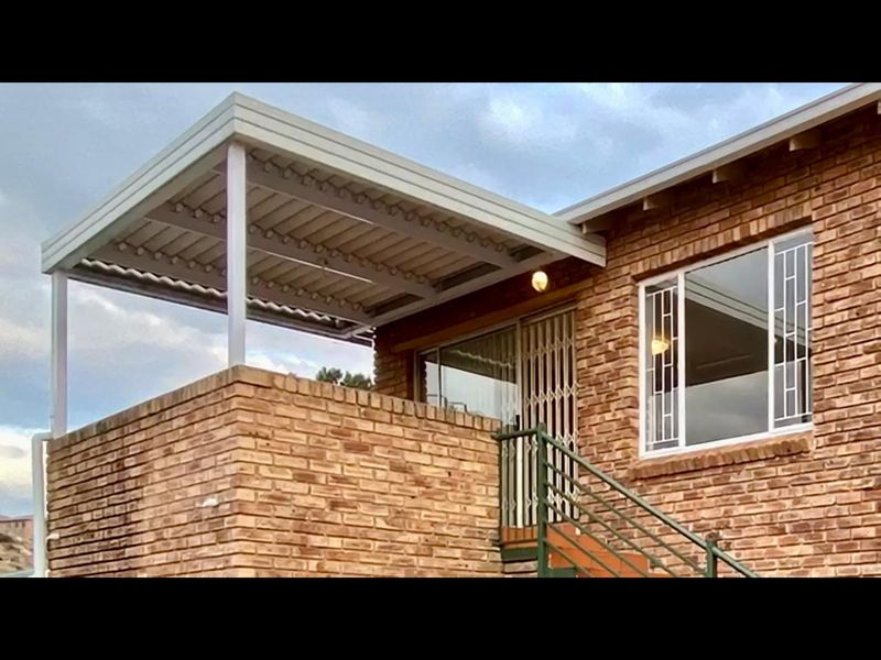 An elevated brick townhouse balcony featuring a covered pergola, security gate, and external staircase access.