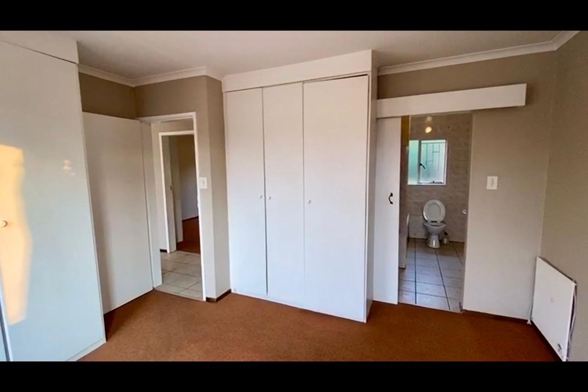 A spacious bedroom featuring built-in cupboards, neutral wall finishes, and direct access to an en-suite bathroom.