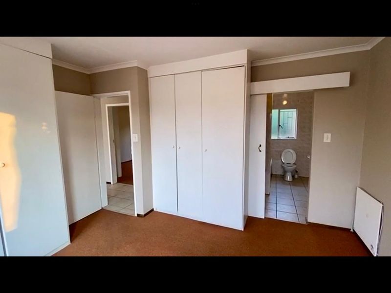 A spacious bedroom featuring built-in cupboards, neutral wall finishes, and direct access to an en-suite bathroom.