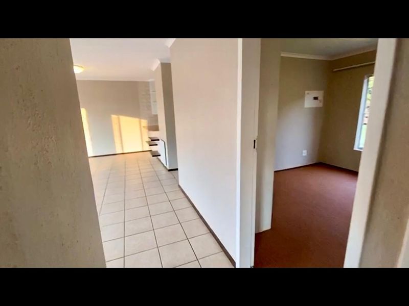 A view from the hallway looking into an open plan living area and an adjacent bedroom with neutral wall finishes and mixed flooring.