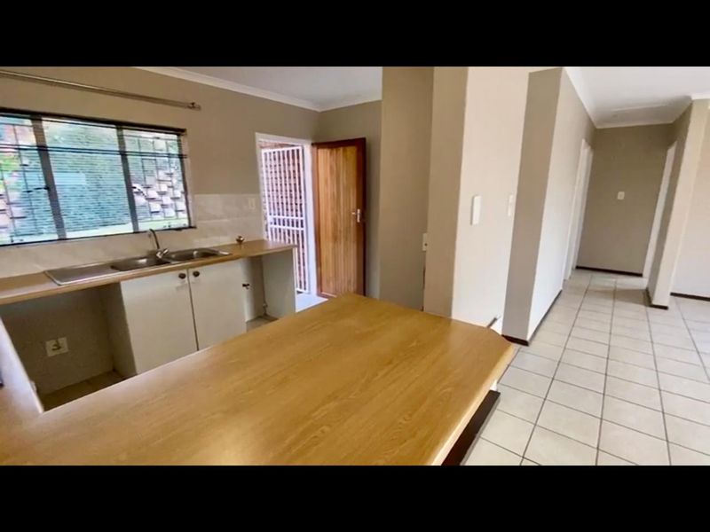 A functional kitchen area featuring tiled flooring, laminate countertops, a double sink, and direct access to an exterior security gate.
