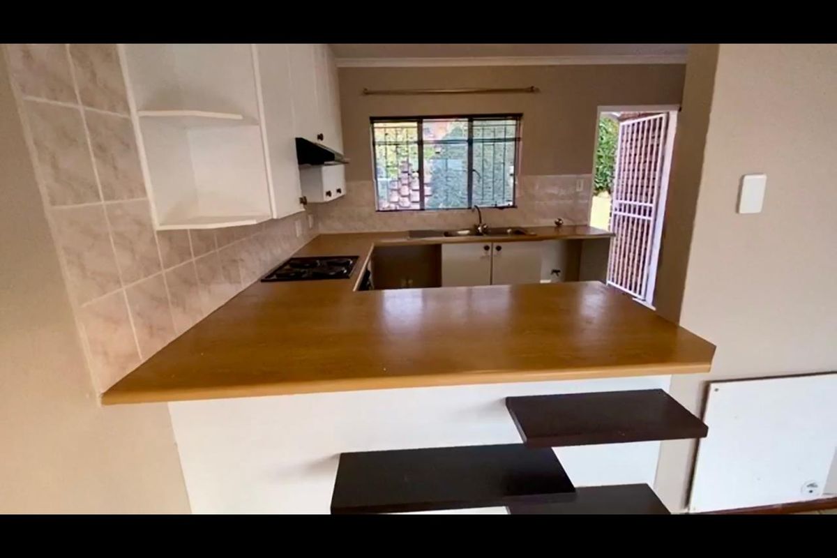 A functional kitchen featuring built-in cabinetry, laminate countertops, a hob, and a double sink, with direct access to the exterior via a security gate.