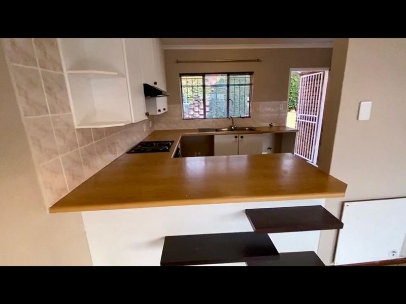 A functional kitchen featuring built-in cabinetry, laminate countertops, a hob, and a double sink, with direct access to the exterior via a security gate.