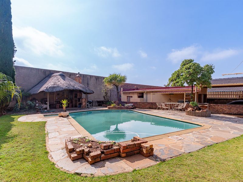 Outdoor pool area featuring a swimming pool, stone paving, and a thatched lapa with a built-in braai, set within a private garden.