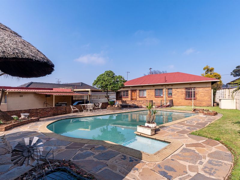 Outdoor pool area featuring a swimming pool, stone paving, and a thatched lapa, set within a private backyard with brick boundary walls.