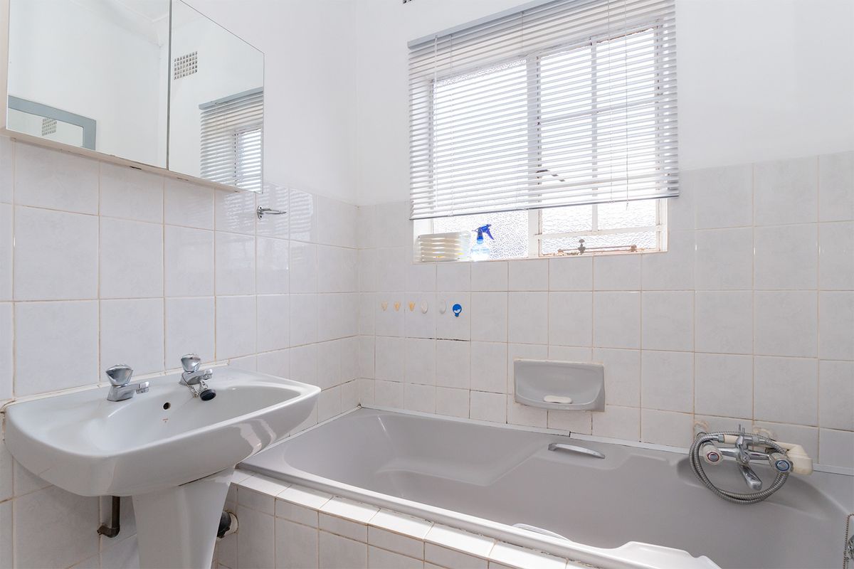 A functional bathroom featuring a pedestal basin, built-in bathtub with shower mixer, and tiled wall finishes.