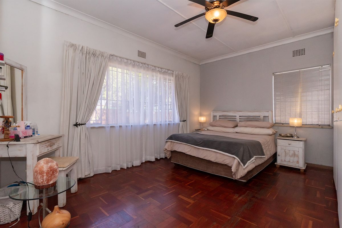 Spacious bedroom featuring warm parquet flooring, a central ceiling fan, and built-in storage, offering a comfortable and functional living space.