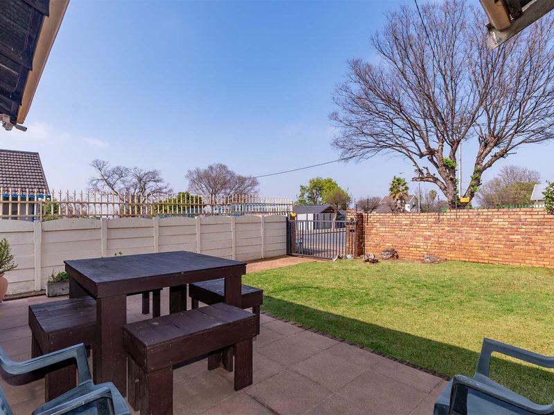 A paved outdoor patio area featuring a brick and precast concrete boundary wall with secure metal gate access to the garden.