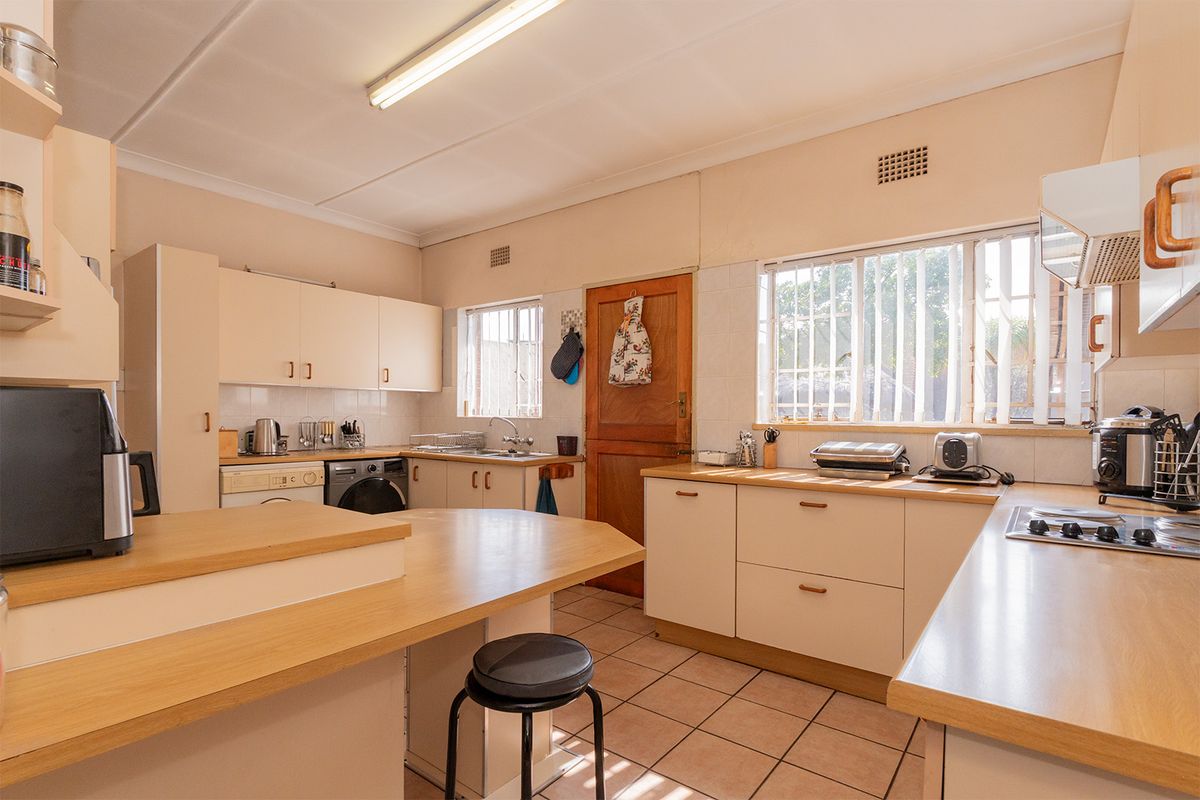 A functional kitchen featuring ample built-in cabinetry, laminate countertops, a built-in hob, and tiled flooring with natural light from multiple windows.