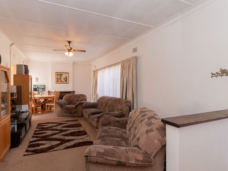 Open-plan living and dining area featuring neutral walls, carpeted flooring, and a ceiling fan, providing a functional and versatile living space.