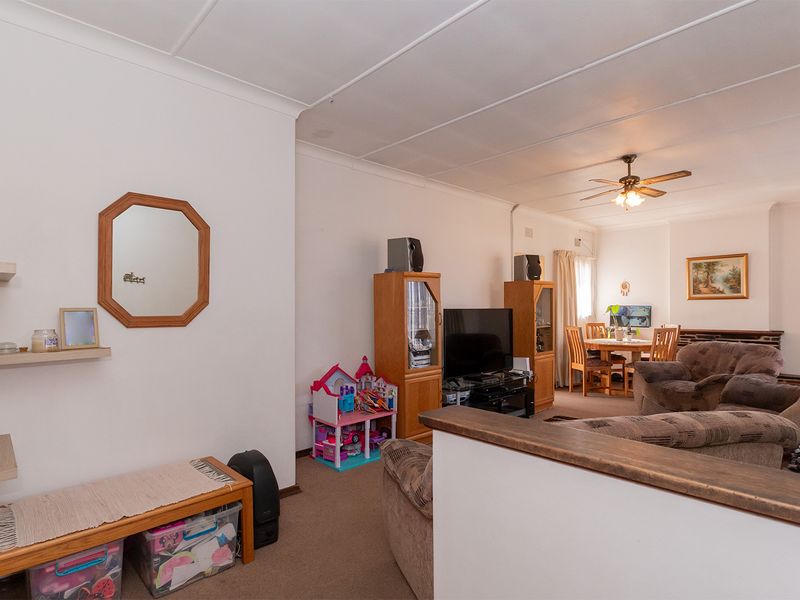 Open plan living and dining area featuring carpeted flooring, a ceiling fan, and a partition wall separating the spaces.
