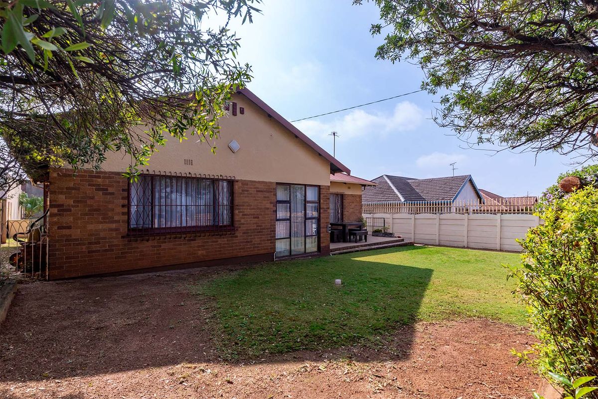 Rear view of the property featuring a brick facade, security bars on windows, a paved patio area, and a private garden with boundary walling.