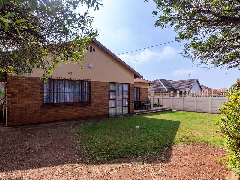 Rear view of the property featuring a brick facade, security bars on windows, a paved patio area, and a private garden with boundary walling.
