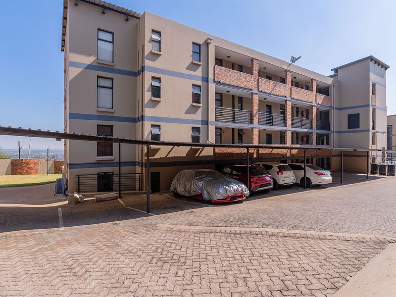 Exterior view of an apartment complex featuring a paved driveway and covered parking bays for residents.