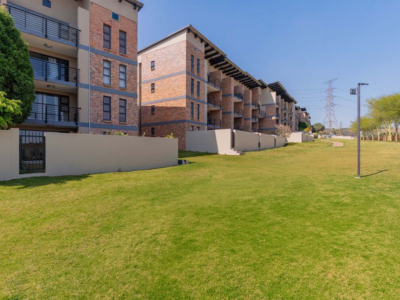 A view of the rear facade of the apartment complex, featuring face-brick construction, private balconies, and well-maintained communal lawn areas.