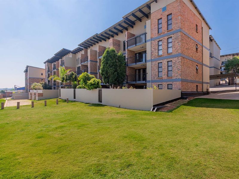 Exterior view of a modern apartment complex featuring brick facade architecture, private balconies with metal railings, and a well-maintained communal lawn area.