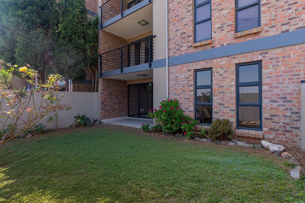 Rear view of the apartment building featuring an exposed brick facade, a private ground-floor patio, and a small landscaped garden area.