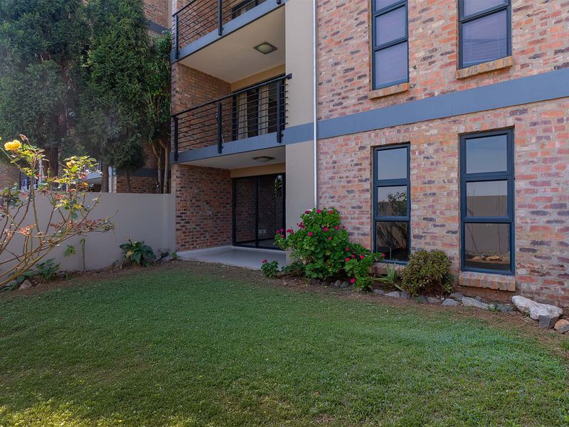 Rear view of the apartment building featuring an exposed brick facade, a private ground-floor patio, and a small landscaped garden area.