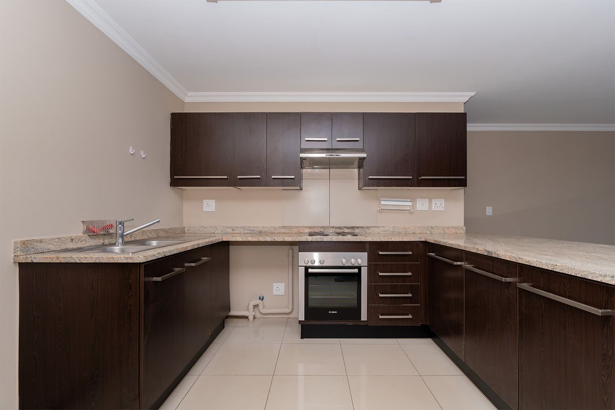 A clean, modern kitchen featuring dark wood cabinetry, granite countertops, built-in oven, electric hob, and tiled flooring in an open-plan layout.