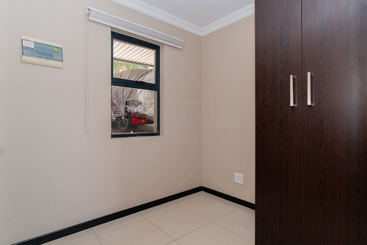 A clean, empty bedroom featuring neutral walls, tiled flooring, and a dark wood built-in wardrobe with modern handles.