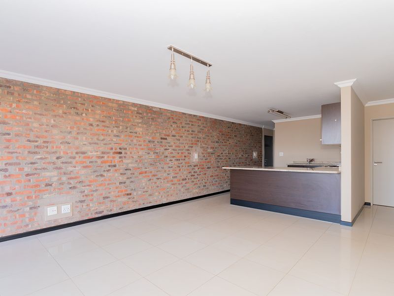 Spacious open-plan living area featuring a striking exposed brick feature wall, tiled flooring, and a functional kitchen with a breakfast bar.