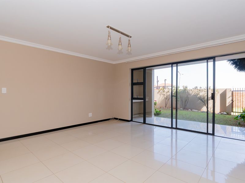 Spacious, empty living area featuring neutral tiled flooring, modern pendant lighting, and large sliding glass doors providing access to the rear garden.
