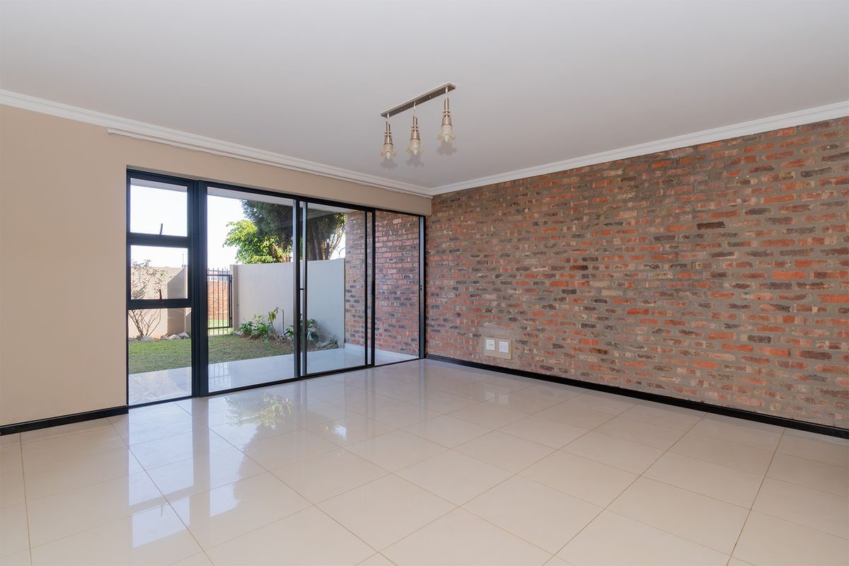 Spacious living area featuring a striking exposed brick wall, polished tile flooring, and large sliding glass doors providing direct access to the garden.