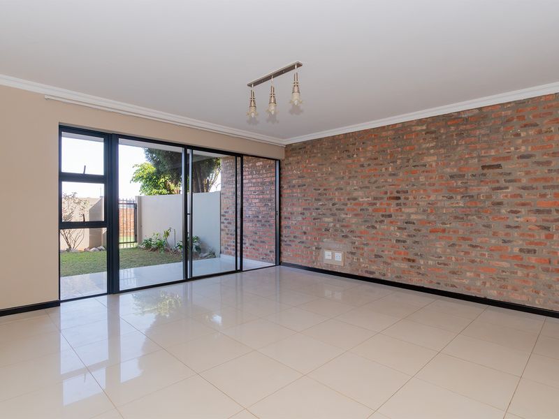 Spacious living area featuring a striking exposed brick wall, polished tile flooring, and large sliding glass doors providing direct access to the garden.