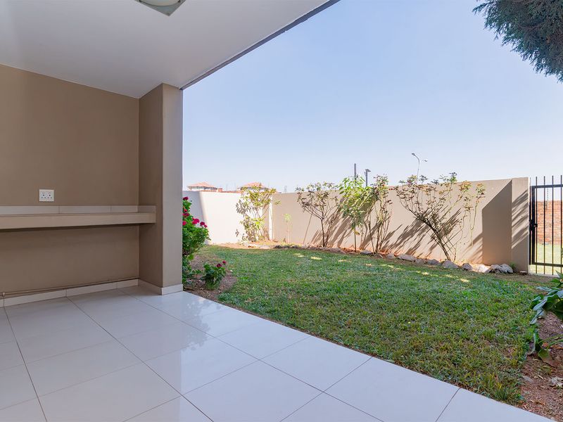 A covered patio area featuring tiled flooring and a built-in counter, overlooking a private garden with a boundary wall and gated access.