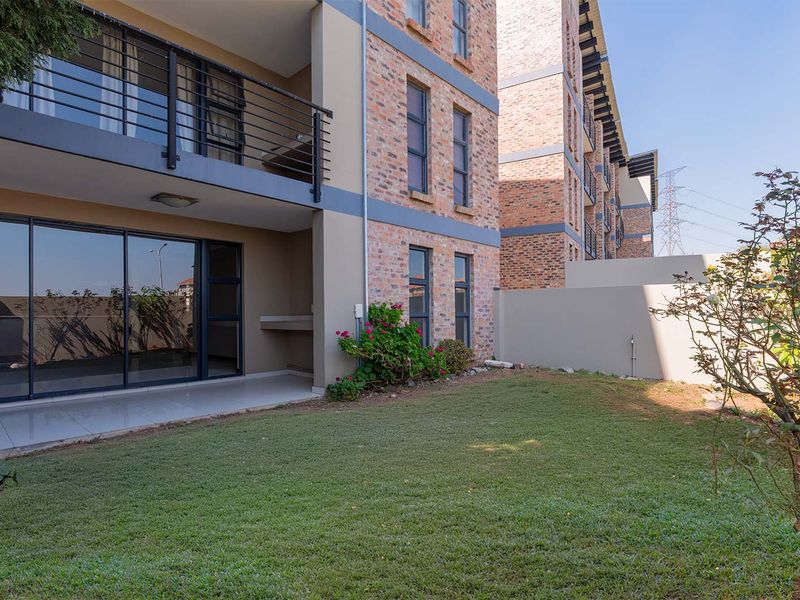 Rear view of the apartment building featuring a private garden, tiled patio with a built-in braai, and access via sliding glass doors.