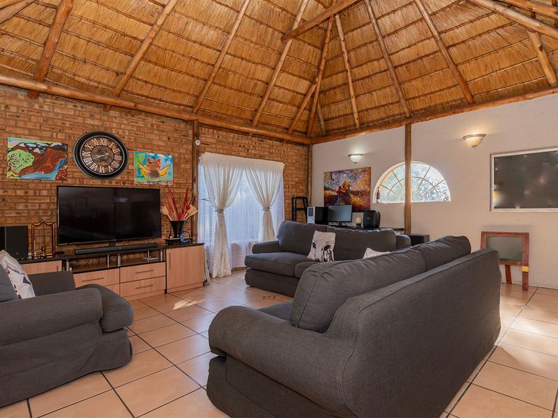 Spacious living room featuring a high vaulted thatched ceiling, exposed brick walls, and tiled flooring, creating a rustic and inviting atmosphere.