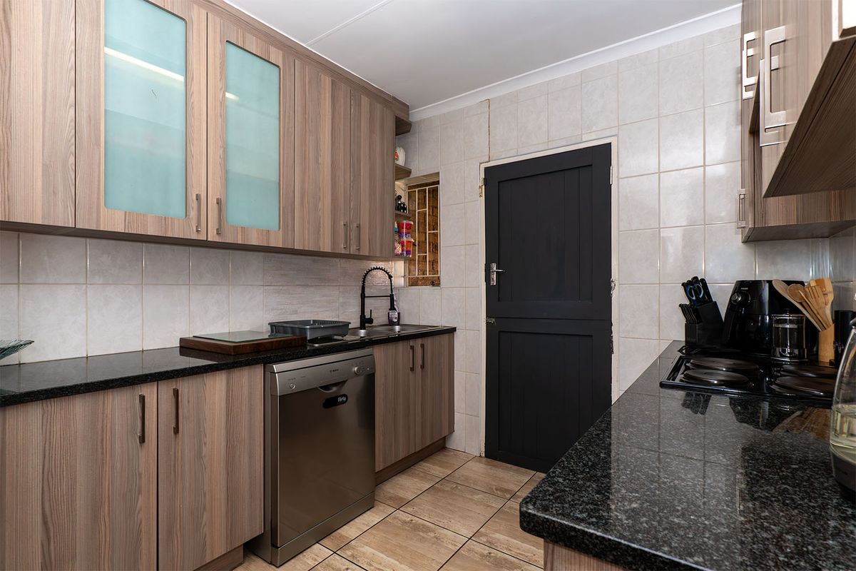 A functional kitchen featuring wood-look laminate cabinetry, dark granite countertops, tiled backsplash, and ceramic flooring with a convenient side door access.