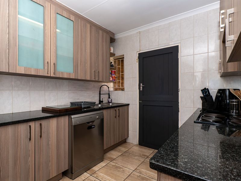 A functional kitchen featuring wood-look laminate cabinetry, dark granite countertops, tiled backsplash, and ceramic flooring with a convenient side door access.