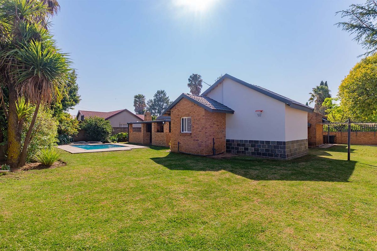 A spacious rear garden featuring a swimming pool, well-maintained lawn, and a brick-built house with a tiled roof and stone-clad base.