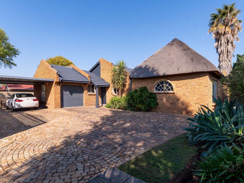 Front exterior view of a brick house featuring a combination of thatched and tiled roofing, a paved circular driveway, and a covered carport.
