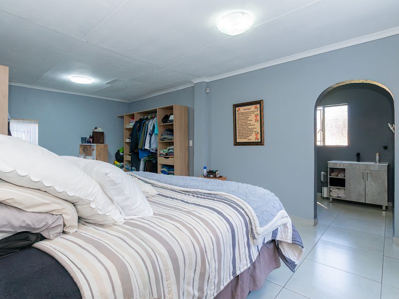 Spacious bedroom featuring tiled flooring, an arched entryway leading to an en-suite vanity area, and functional ceiling lighting.