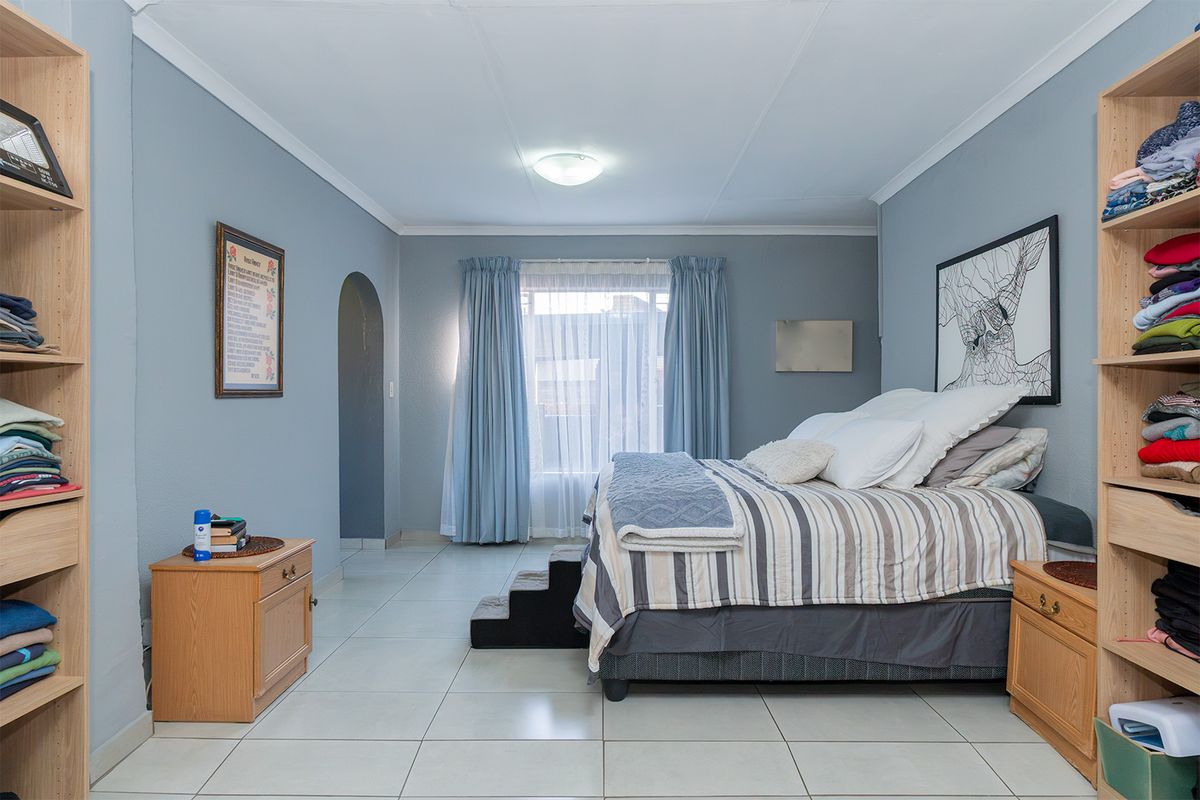 A spacious bedroom featuring light blue walls, tiled flooring, and dual built-in shelving units flanking the sleeping area.