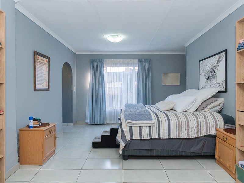 A spacious bedroom featuring light blue walls, tiled flooring, and dual built-in shelving units flanking the sleeping area.