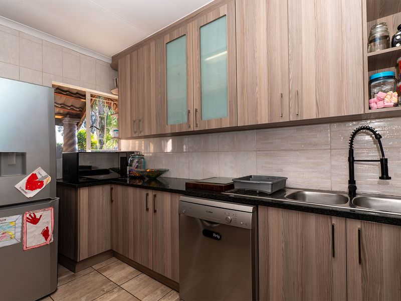 A functional kitchen featuring wood-look laminate cabinetry, granite countertops, a double bowl sink with a modern faucet, and tiled backsplash.