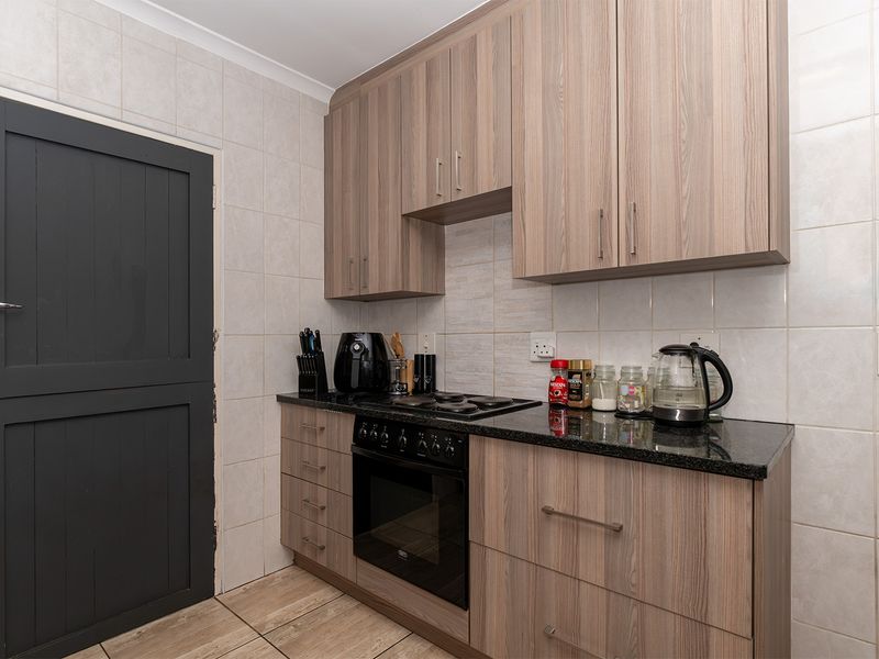 A compact kitchen featuring wood-look cabinetry, granite countertops, a built-in oven with hob, and full-height wall tiling.