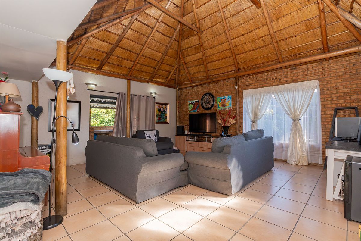 Spacious living room featuring a high thatched ceiling with exposed timber rafters, exposed brick walls, and neutral ceramic floor tiles.
