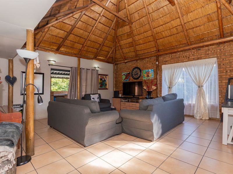 Spacious living room featuring a high thatched ceiling with exposed timber rafters, exposed brick walls, and neutral ceramic floor tiles.