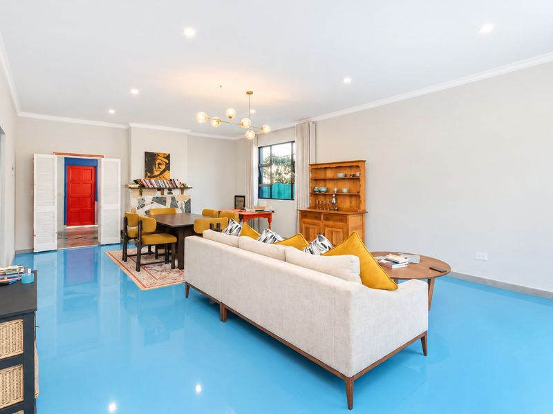 Spacious open-plan living and dining area featuring distinctive glossy blue epoxy flooring, a stone-clad fireplace, and recessed lighting throughout.