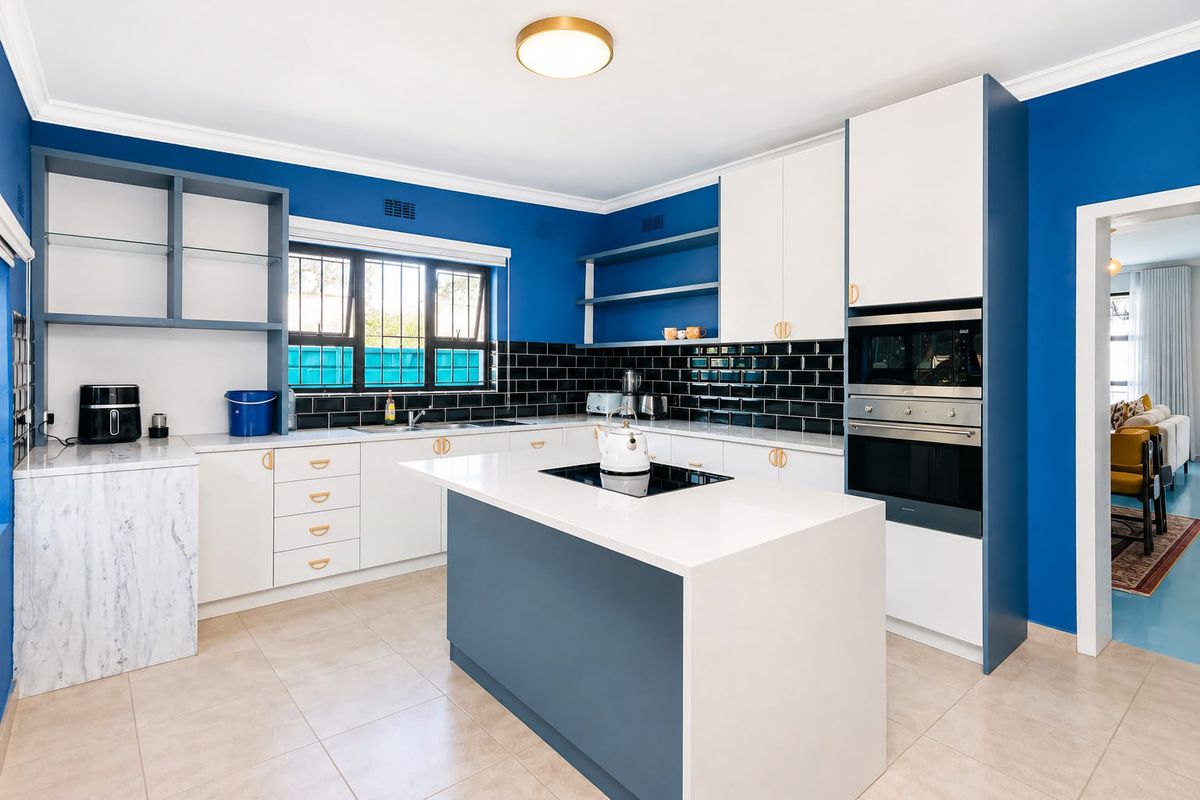 Modern kitchen featuring a central island with induction cooktop, built-in oven and microwave, sleek cabinetry, and a striking blue accent wall.