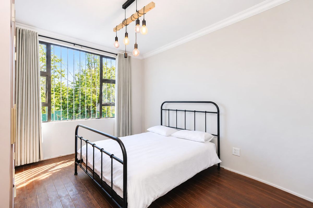 A bright bedroom featuring timber flooring, security bars on the window, and modern pendant lighting.