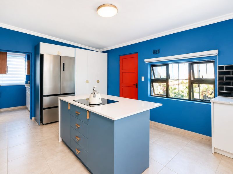 Modern kitchen featuring a central island with a cooktop, sleek cabinetry, tiled backsplash, and bright blue walls with a contrasting red door.