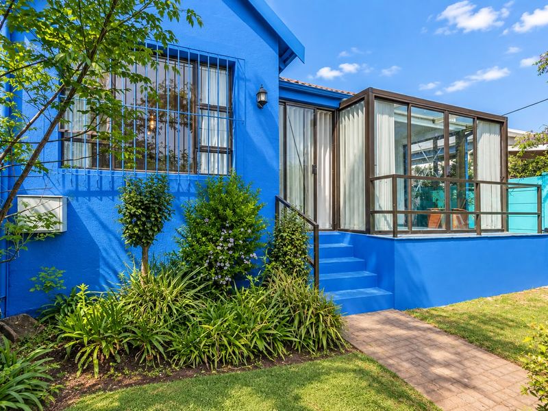 Rear exterior view featuring a vibrant blue facade, an enclosed patio area with glass sliding doors, and a paved garden walkway.